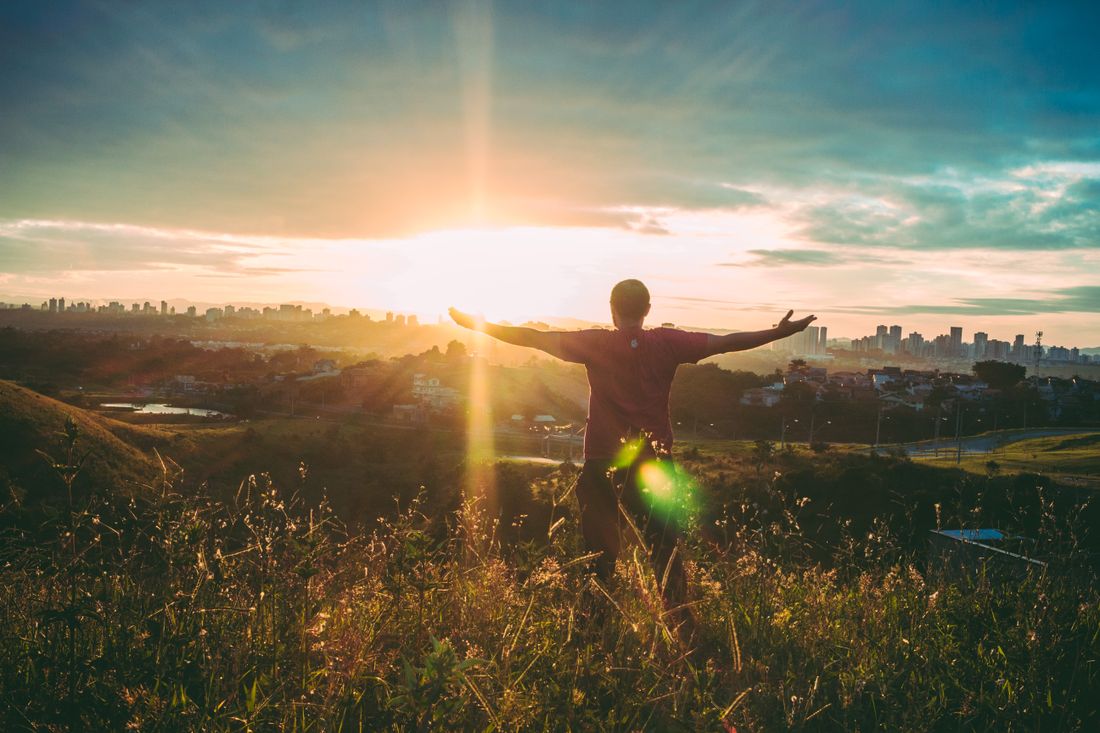 A man with arms open to the rising sun on a grassy hill
