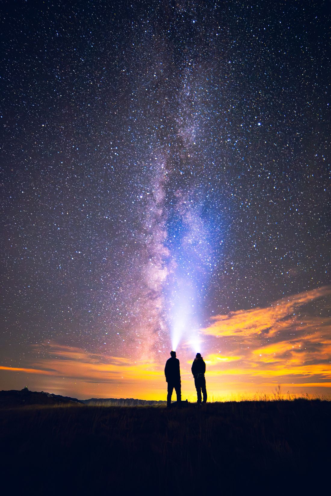 Two people under the Milky Way, shining headlamps into the sky